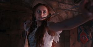 Above angle shot of Joey King, star of 20th Century Studios’ The Princess, holding a rope and wearing the remnants of her white wedding gown.