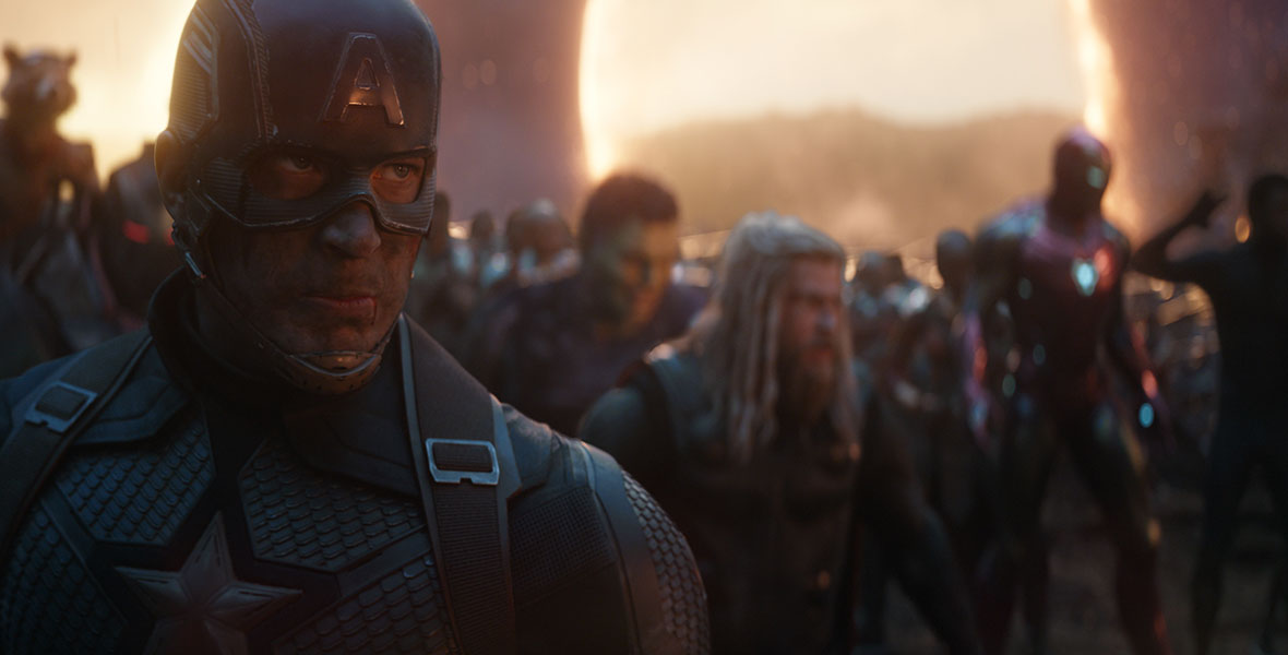 In this scene from Avengers: Endgame, Chris Evans’ Captain America is in the foreground. His face is dirty and his helmet is scuffed, but his face has a determined expression.