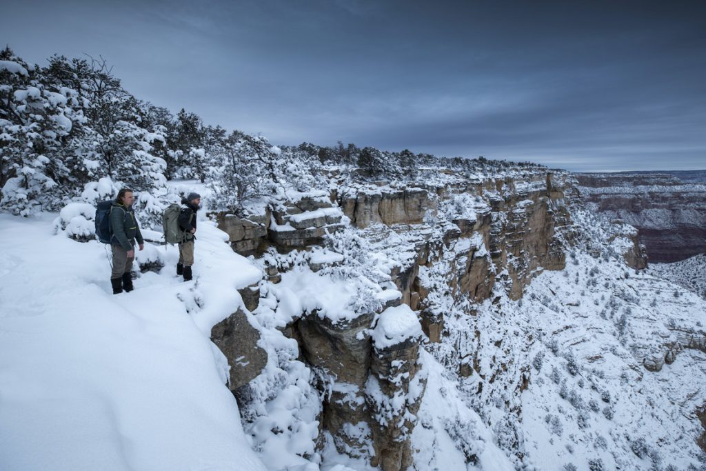 In a scene from National Geographic’s America the Beautiful on Disney+, wildlife cameramen Jake Davis and Pete Matthews survey the Grand Canyon, Arizona, after heavy snowfall, on a hike to check and maintain camera traps deployed along its rim.