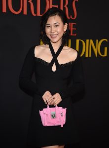 Christine Koon on the red carpet at the premiere of Hulu’s Only Murders in the Building season 2. She’s wearing a black dress and holding a small pink purse. The logo for the show is seen behind her.