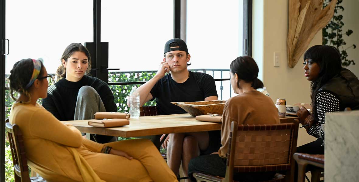 Five contestants on ABC’s Claim to Fame sit at a dining room table, talking