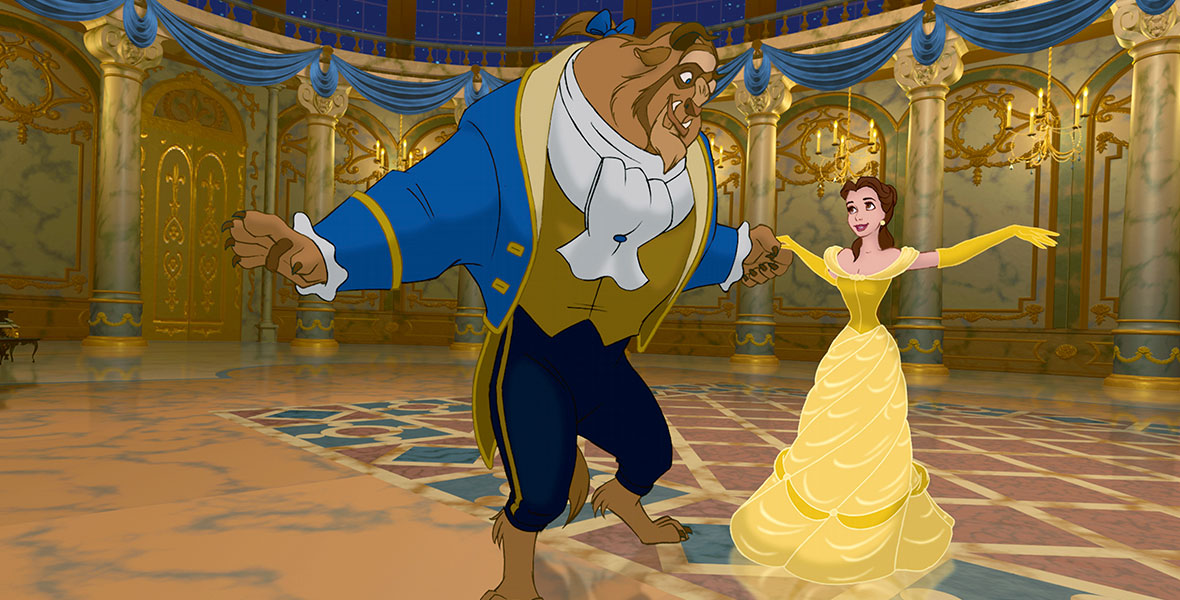 In a still from Disney’s Beauty and the Beast, the Beast and Belle are dancing in the Beast’s ballroom. He is wearing a blue tailcoat and gold vest; she is wearing her signature gold ballgown. The room is surrounded by candelabras and blue bunting, and through the windows at the top of the room you can see the star-filled night sky.