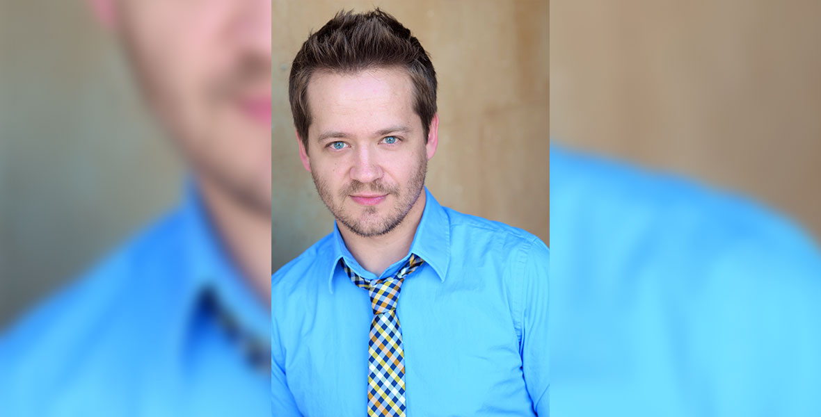 A headshot image of Jason Earles. He has short brown hair styles into a point at his forehead. He has some stubble and bright blue eyes. He is wearing a bright blue, almost cyan, dress shirt and a checkered blue and yellow tie.