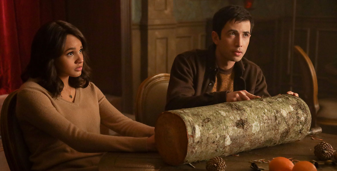 Actress Ashley Nicole Williams and Actor Tony Giroux sit at a wooden dining table that’s topped with a large log and oranges.