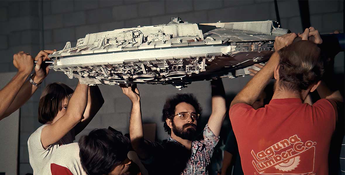 A group of men, including Disney Legend George Lucas, carry a model of the Millennium Falcon