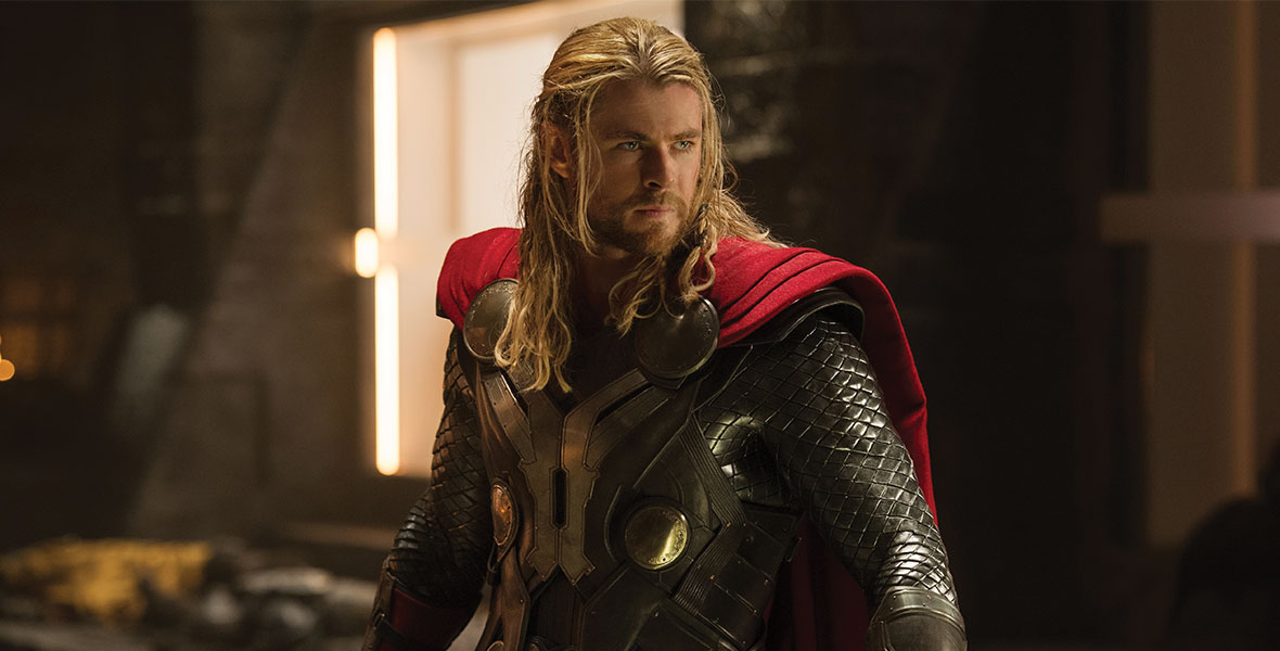 Thor stands looking off in his long-sleeved armor and red cape, with hammer in hand.