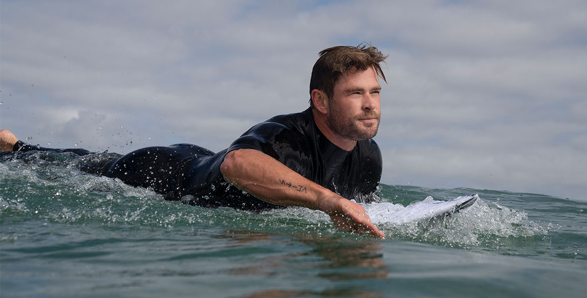 Actor Chris Hemsworth lays on a surfboard as he paddles across the ocean in Shark Beach with Chris Hemsworth.