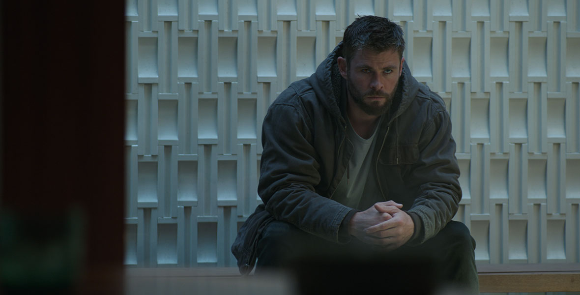 Chris Hemsworth as Thor sits on a bench in front of a white stone wall, with his hands resting on his knees, in Marvel Studios’ Avengers: Endgame.