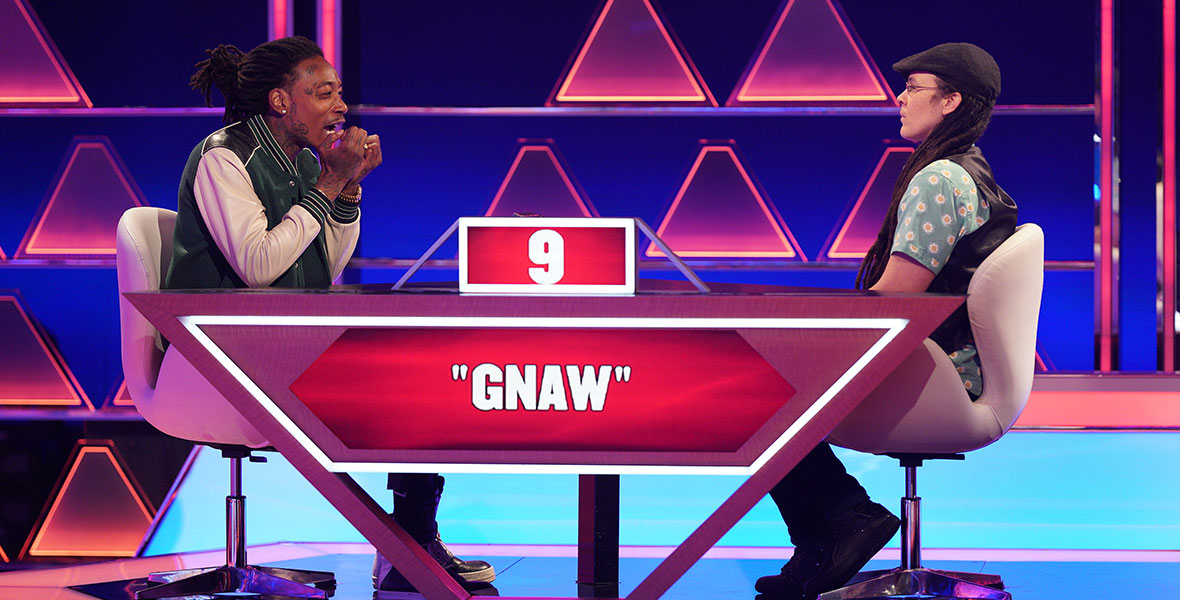 (L-R) Recording artist Wiz Khalifa sits at a table across from a contestant as he attempts to act out the word “gnaw” on the game show The $100,000 Pyramid.