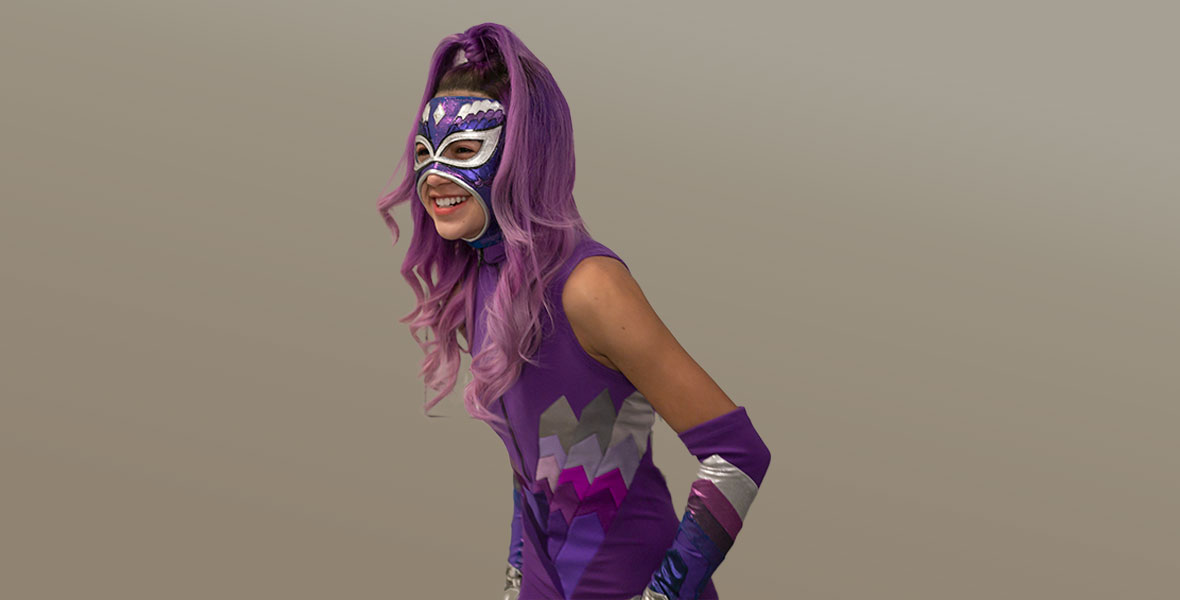 Actress Scarlett Estevez laughs while wearing a neon purple luchadora costume adorned with silver accents