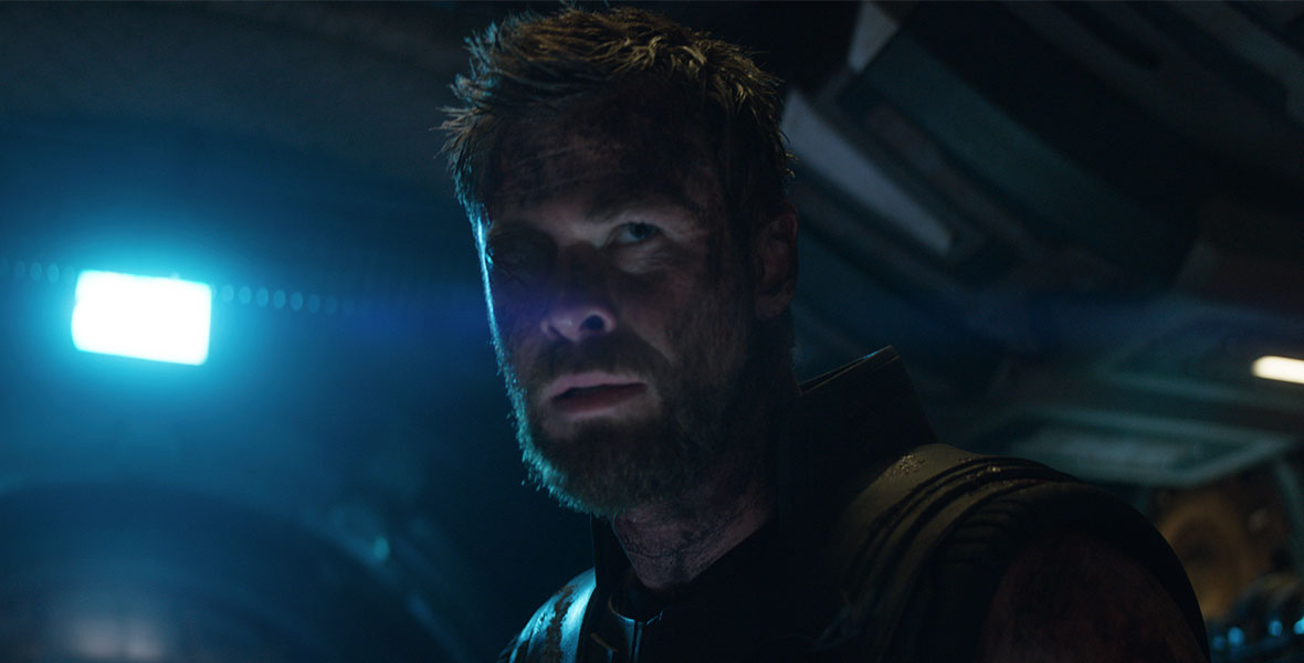 A bright blue light lights up the right side of Hemsworth’s face in a close-up headshot.