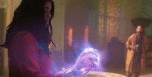 Kamala Khan, aka Ms. Marvel, is shown in profile as she displays her illuminated and enlarged fist to Waleed, a new character and mentor to the Red Daggers, who stands in the background in a darkened sanctuary.