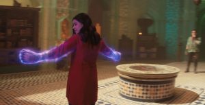 Kamala Khan, aka Ms. Marvel is seen from the back, as she stands and displays her illuminated and enlarged fists to Waleed, a new character and mentor to the Red Daggers, and Kareem, a member of the Red Dagger society in their darkened, book-filled sanctuary.