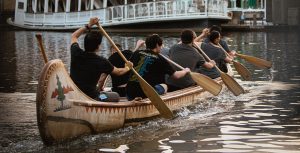A crew paddles around Tom Sawyer Island at Disneyland Park, with the Mark Twain Riverboat visible in the distance shortly after sunrise as part of the Disneyland Resort Canoe Race time trials.