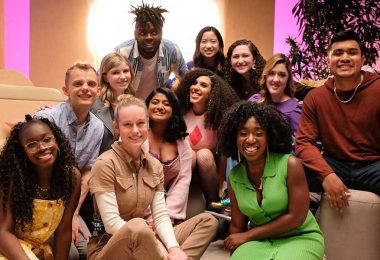 The Heroes and stars of Growing Up—Alex Crotty; Clare Della Valle and Isabel Lam; Amiri Nash; Athena Nair; Sofia Ongele; Emily Flores; Sage Grace Dolan-Sandrino; Gavin Arneson; Vanessa Aryee; and David Puma—gather around creator, executive producer, and director Brie Larson. Tan pillows and shapes are seen behind them, along with a leafy potted plant and bright light.