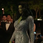 Actor Tatiana Maslany portrays Jennifer Walter/She-Hulk with CGI green skin and hair. She is walking while wearing a silver beaded ballgown.