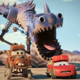 In an image from the Disney+ series Cars on the Road, the brown tow truck Mater is on the left and the red sports car Lightning McQueen is on the right. They’re being chased by some sort of purple dinosaur-car hybrid with large wheels through a desert landscape.