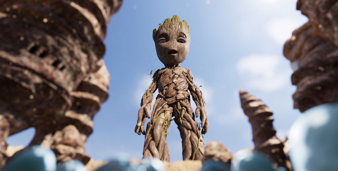Against a blue sky, Baby Groot is standing, mouth agape, and looking down at out-of-focus blue insects. He is surrounded by desert spires.
