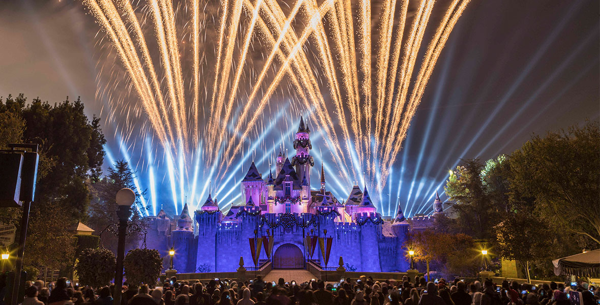 Golden fireworks crackle over Sleeping Beauty’s Winter Castle during the “Believe... in Holiday Magic” nighttime spectacular. The castle is illuminated in blue and purple lights as dozens of guests stand before it.