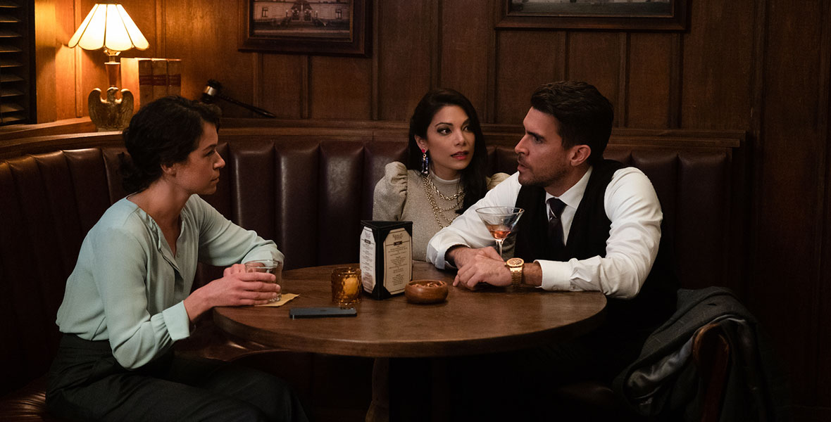 (Left to Right) Actors Tatiana Maslany, Ginger Gonzaga, and Josh Segarra sit around a large wooden table in a corner booth. On the table are beverages and a triangular menu. Behind them, three photos of buildings are hung in brown frames.