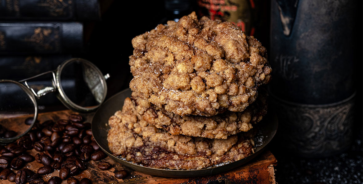 A stack of large, crumbly cookies sits on a small brown plate. The plate is on top of a antique orange book with a pair of glasses.