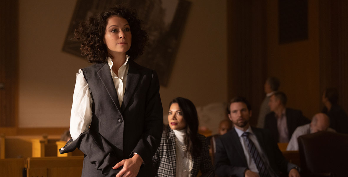 Actor Tatiana Maslany as Jennifer Walters/She-Hulk stands in court with a suit sleeve torn, and Ginger Gonzaga as Nikki Ramos looks on from a chair.