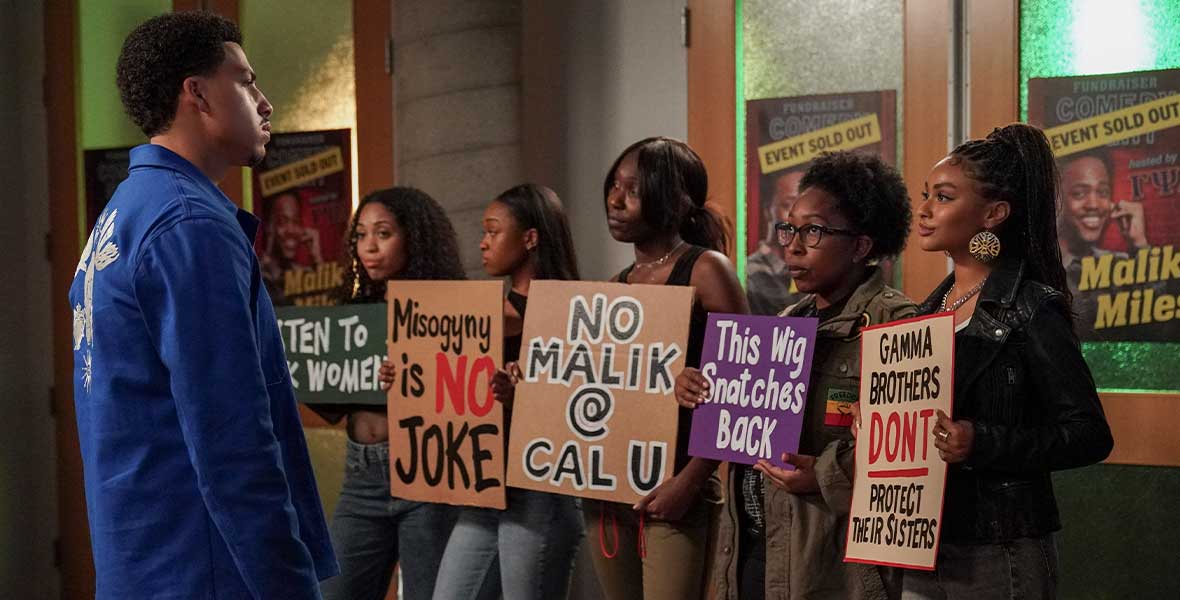 (Left to right) Actor Marcus Scribner looks at a group of five women holding colorful protest signs outside of a theatre