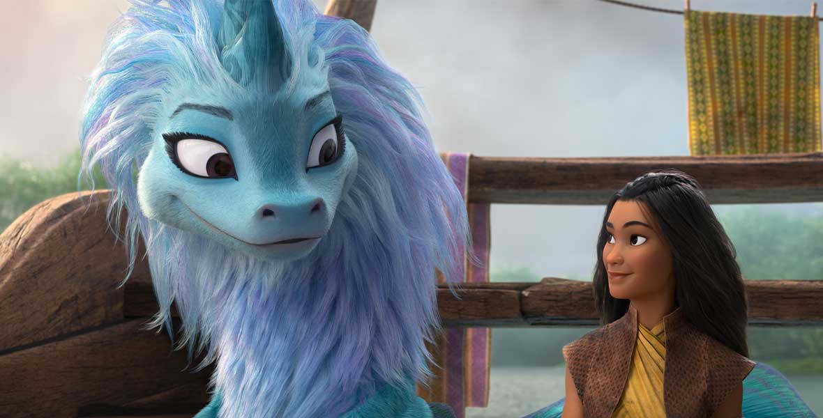 Raya looks adoringly at a dragon. She is wearing a yellow top and dark brown vest. The dragon is multi-colored with light blue and purple fur.