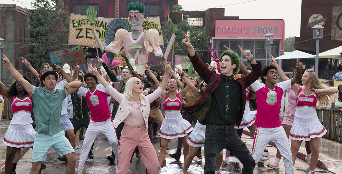 Actors (Left to right) Trevor Tordjman, Meg Donnelly, Milo Manheim, and Noah Zulfikar dance with their arms in the air with a crowd of Seabrook students behind them.