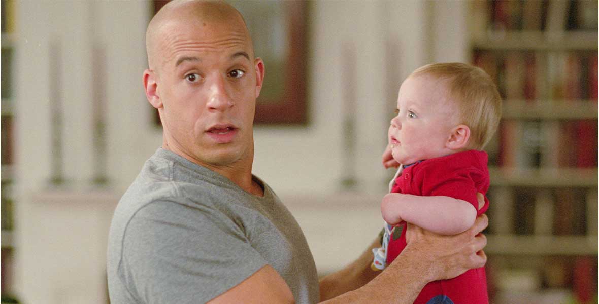 Actor Vin Diesel wears a grey T-shirt and holds a male infant