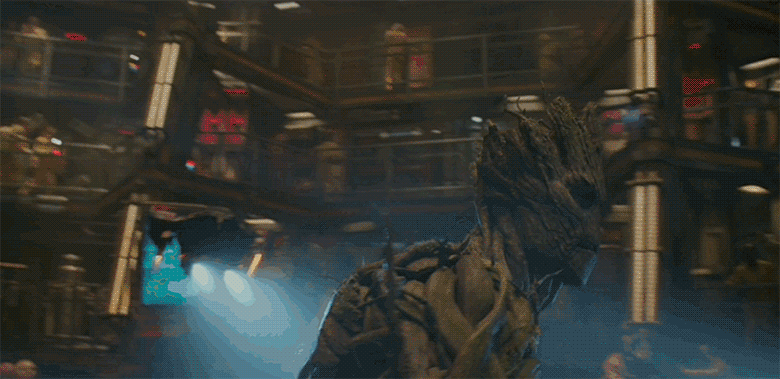 A gif of adult Groot from Guardians of the Galaxy. He is in the jail compound and large flying robots circle around him before he screams into the camera and flickering lights illuminate his menacing face.