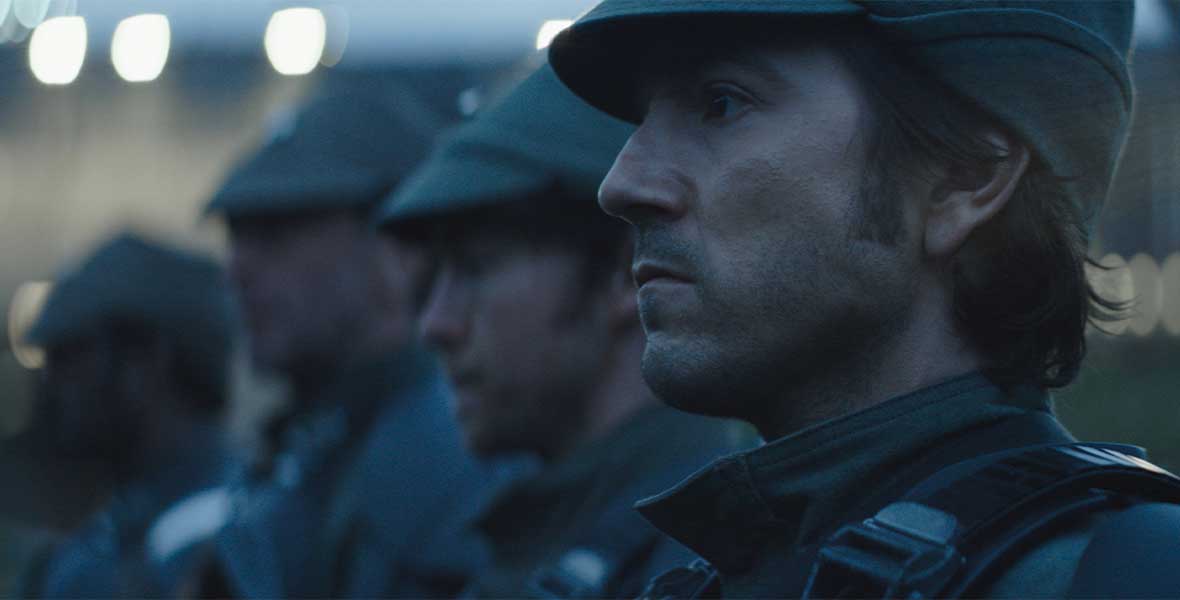 Diego Luna as Cassian Andor stands in a line of Imperial soldiers, all looking to the left with a serious expression.
