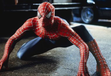 Spider-Man crouches down in his red and blue spidey suit, looking ready to pounce. His hands and knees are touching the asphalt.