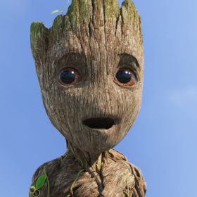 A close-up of young, adolescent age Groot. He is looking past the camera with a happy, but surprised look on his face. His eyes are wide and his mouth is slightly agape. Behind him is a bright blue sky with a few fluffy white clouds.