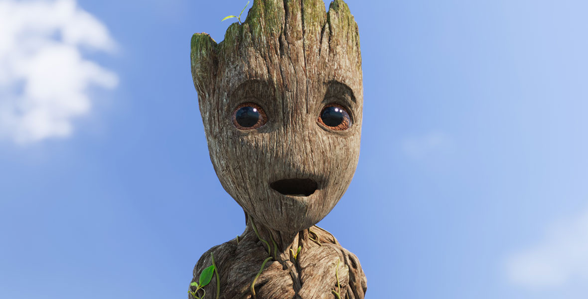 A close-up of young, adolescent age Groot. He is looking past the camera with a happy, but surprised look on his face. His eyes are wide and his mouth is slightly agape. Behind him is a bright blue sky with a few fluffy white clouds.
