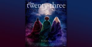 The front cover of Disney twenty-three, featuring the publication logo above the backs of Sarah, Winnifred, and Sarah Sanderson, all wearing cloaks and standing on a wooded hill overlooking a town at night. The text below them states, “We’re back, witches.”