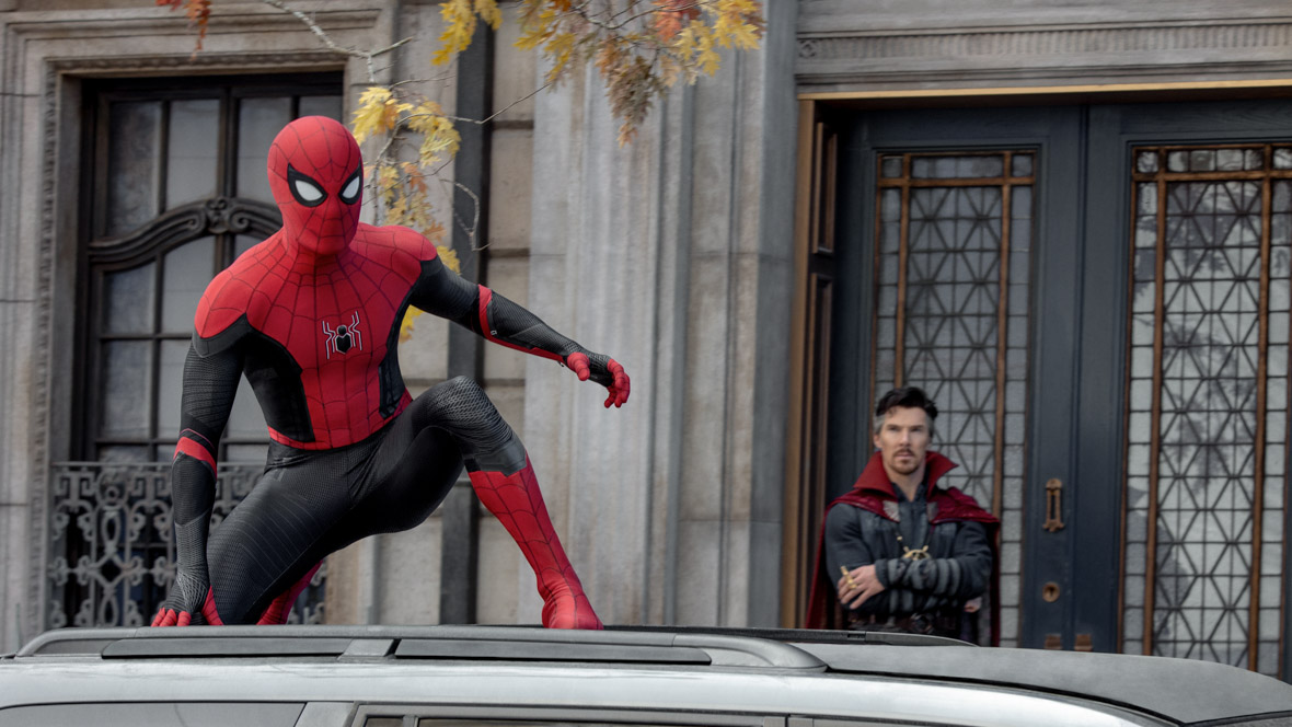 Spider-Man wears a red and black Spider suit crouched on top of a car. Doctor Strange is in the background with his arms crossed in a black armored suit with a red cape.