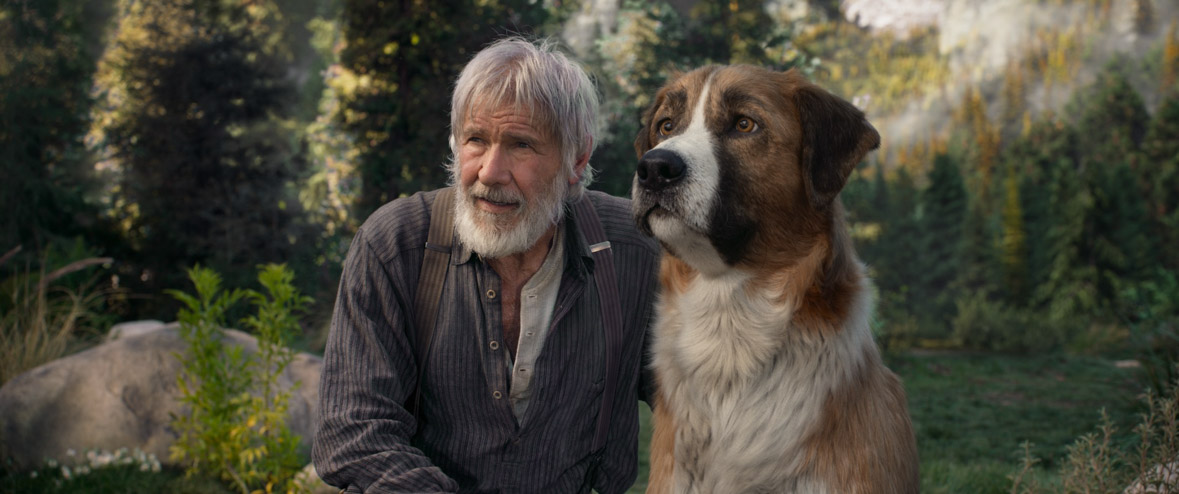 John Thornton, played by a bearded Harrison Ford, kneels beside his dog, Buck, in a grassy field.