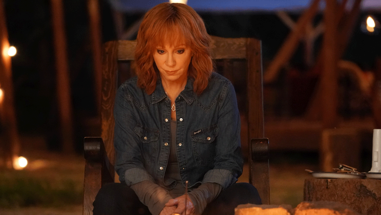 Reba McEntire, in character as Sunny Barnes, wears a denim shirt and sits in a wooden rocking chair in front of a bonfire. She has red, shoulder-length hair and a pensive look on her face.