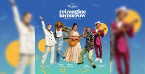 OTNES stands on the far left, wearing an oversized white suit, a brown shirt, and white platform shoes. Her right hand is extended in the air, and she is smiling. Next to them is Gabby Samone, who is wearing a checkered jacket, distressed denim pants, a white tank top, and white sneakers. She is smiling and looking upward, and her left arm is extended backward; it’s as if she’s been photographed mid-turn. In the center is Brittney Mendoza, who is wearing a white tank top underneath a corseted cream gown. She is smiling and strumming an acoustic guitar. Next to her is Danni Cassette, who is wearing a black and white floral shirt and green cargo pants. Danni is dancing, with their right arm raised and their knees bent. On the far right is Alan Eugene Price, who wears a silk magenta suit and a white hat. He is holding a violin and looking at the strings. Music notes surround the artists, and the words “The Walt Disney Company,” “Reimagine Tomorrow,” and “Where We All Belong” appear overhead.