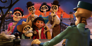 Miguel from Coco stands wearing a red hoodie over a white tank top. His ancestors portrayed by skeletal figures, are standing around him in traditional Mexican clothing.