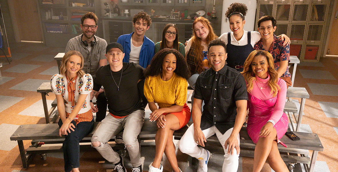 (Back row, from left to right): Tim Federle, Joshua Bassett, Liamani Segura, Julia Lester, Sofia Wylie, Frankie Rodriguez. (Front row, from left to right): Kate Reinders, Lucas Grabeel, Monique Coleman, Corbin Bleu, and Dara Reneé. The cast and crew of High School Musical: The Musical: The Series pose for a group photo on the bleachers in an East High classroom.