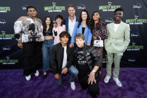 Luke Islam, Taegen Burns, Brady Noon, Josh Duhamel, Lauren Graham, Swayam Bhatia, and DJ Watts stand while Naveen Paddock and Maxwell Simkins kneel on the purple carpet at the premiere of The Mighty Ducks: Game Changers Season 2.