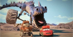 An enormous, animated dinosaur-like car chases Lightning McQueen and Mater through a rural desert landscape. Mater is a brown, vintage tow truck with buck teeth. Lightning McQueen is a red sports car.