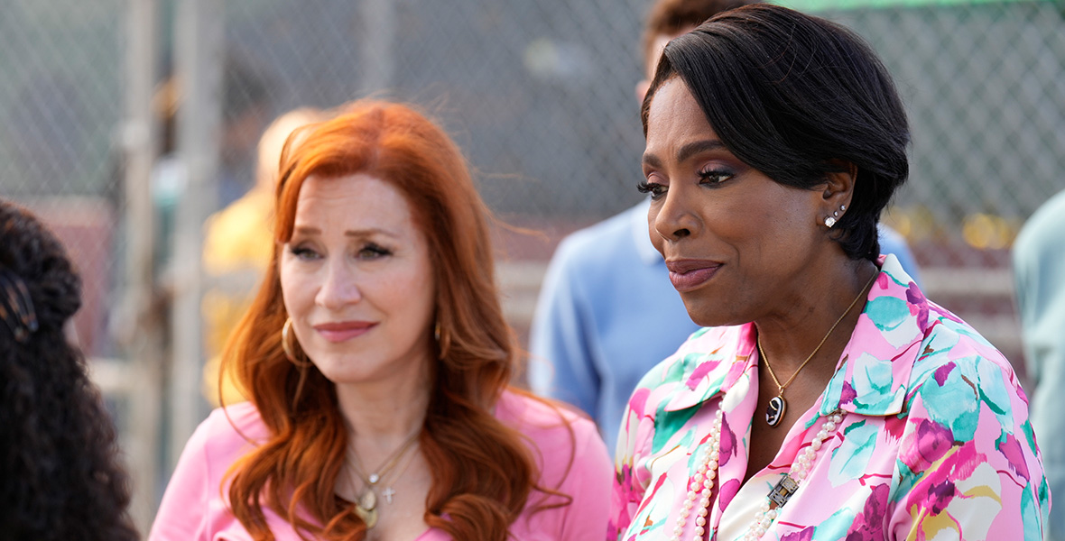 Lisa Ann Walter, in character as Melissa Schemmenti, wears a pink top and layered necklaces. To her left is Sheryl Lee Ralph, in character as Barbara Howard, who is wearing a floral printed top and double strands of pearls. They are talking to Quinta Brunson, in character as Janine Teagues, whose back is to the camera.