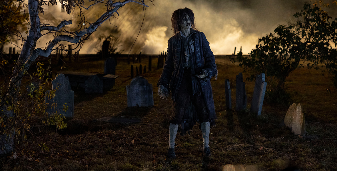 Doug Jones, in character as the zombie Billy Butcherson, stands in a dimly lit graveyard.