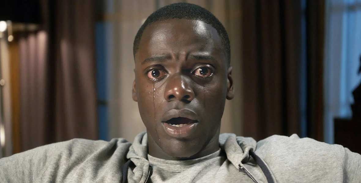 In a still from Get Out, Chris Washington, played by Daniel Kaluuya, sits with his mouth agape. Tears are streaming down his cheeks, as he is frozen in fear.