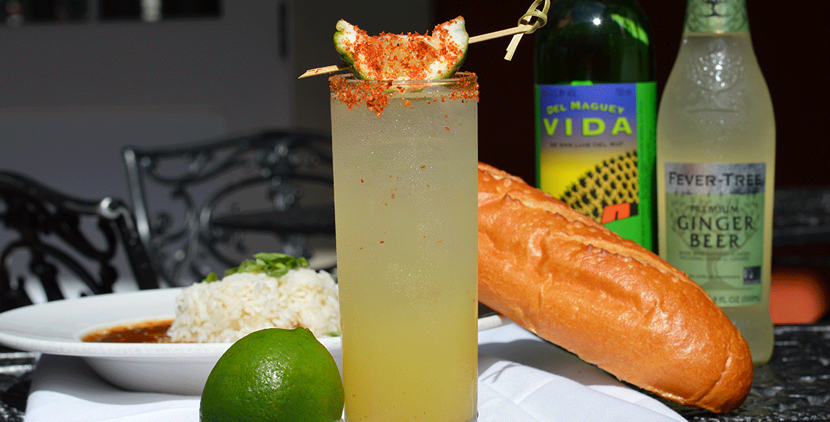 Pina Mezcal Mule topped with a lime placed in front of a plate of beans and rice on a table.