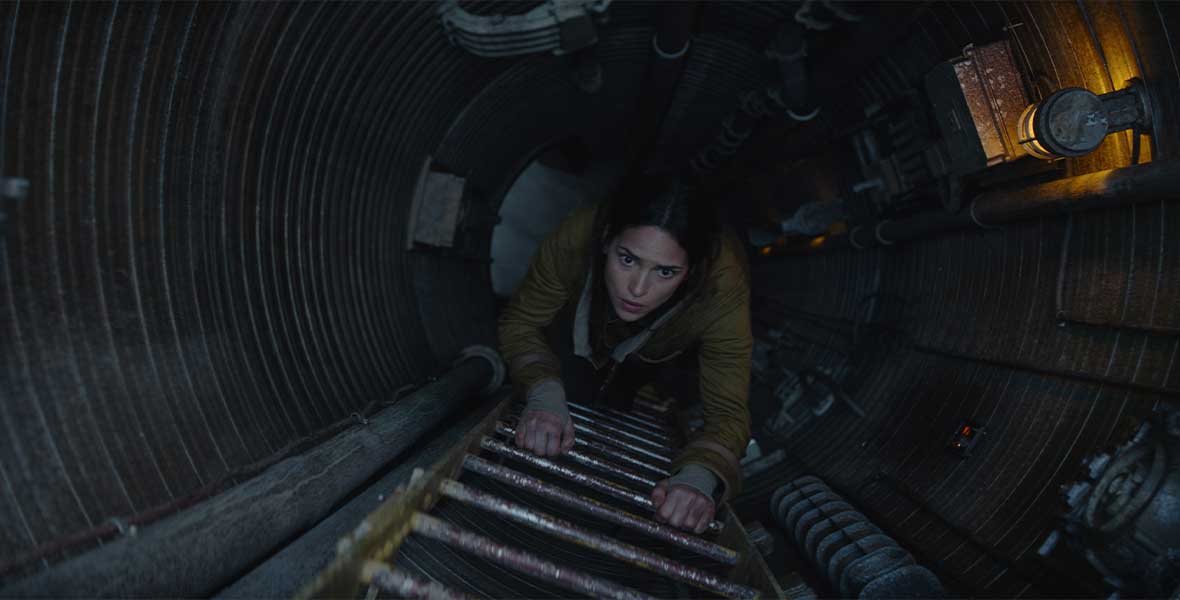 Bix Caleen climbs a ladder in a dark tunnel, look ahead of her as she ascends.