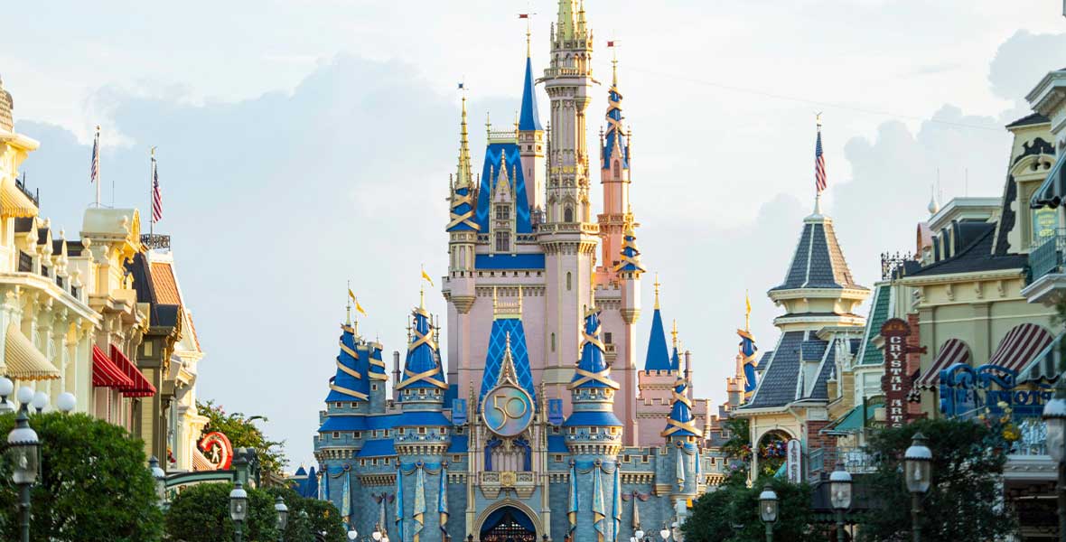 IMAGE 04 Alt Text: Exterior photo of Cinderella Castle at Walt Disney World Resort. On the castle is a large iridescent medallion reading “50,” commemorating the 50th anniversary. Above the castle are light blue skies, and part of Main Street U.S.A. is in the foreground.